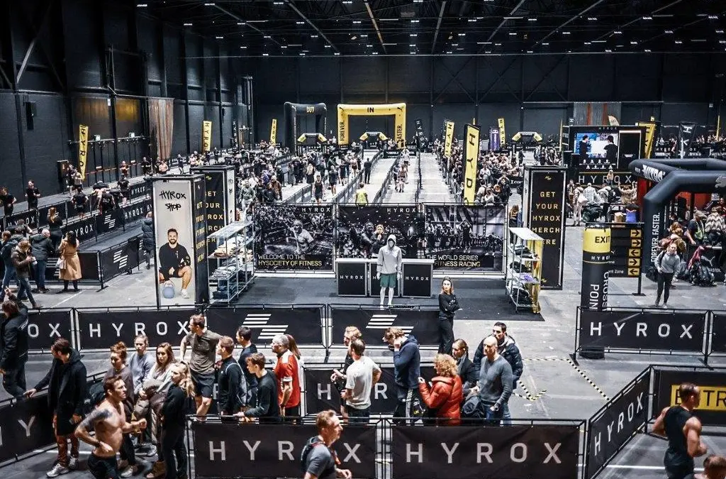 Large-scale HYROX competition event with multiple lanes, crowds of athletes and spectators in a professional arena setting